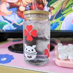 May include: A clear glass bottle with a wooden lid and a straw. The bottle has red clover designs and white cartoon characters on it. The bottle is filled with a clear liquid.