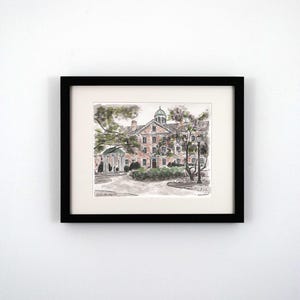 May include: A black framed print of a watercolor illustration of a brick building with a green roof and a cupola. The building is surrounded by trees and a small garden. The text "Old East, UNC Chapel Hill" is printed below the image.