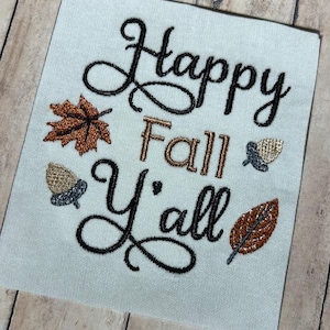 May include: Embroidered design with the text "Happy Fall Y'all" in black cursive font. The design also includes a brown maple leaf, a brown acorn, and a gold acorn.