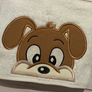 May include: Embroidered brown puppy face with big eyes and a small black nose on a white towel.