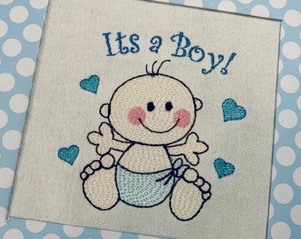 May include: Embroidered white card with blue and pink stitching. The card features a cartoon baby with the text "It's a Boy!"