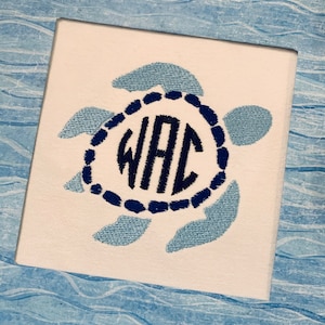 May include: Square white canvas with a light blue embroidered turtle design. The turtle's shell is a dark blue circle with the embroidered letters "WAC" inside. The background has a blue and white wave pattern.