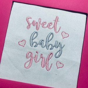 May include: Embroidered white fabric with the text "Sweet baby girl" in pink and gray lettering with pink hearts.