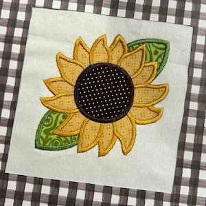 May include: A yellow and brown embroidered sunflower with green leaves. The sunflower has a brown center with white polka dots.