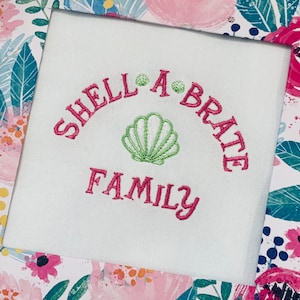 May include: White fabric with pink embroidery that reads "Shell-a-brate Family" with a green seashell in the center.