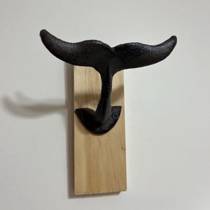 May include: Black cast iron whale tail wall hook mounted on a wooden base.
