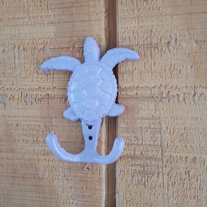 May include: A lavender colored cast iron turtle hook. The hook is shaped like a turtle with a shell and two legs that form a hook.