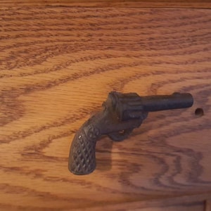 May include: A black metal gun-shaped drawer pull on a wooden surface.