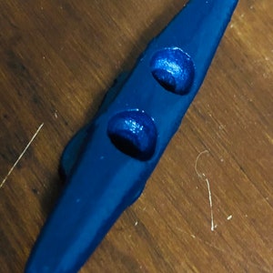 May include: A dark blue nautical cleat with two holes. The cleat is made of plastic and has a smooth finish.