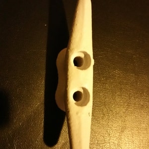 May include: White ceramic cleat with two holes. The cleat is designed for securing ropes or lines.