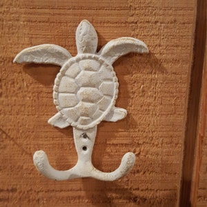 May include: White ceramic sea turtle hook with a double hook design. The hook is mounted on a wooden surface.