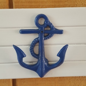 May include: A blue metal anchor with a rope detail, mounted on a white wooden surface.