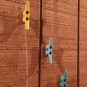 May include: Three decorative hooks in the shape of airplanes mounted on a wooden wall. One hook is yellow, and the other two are light blue.