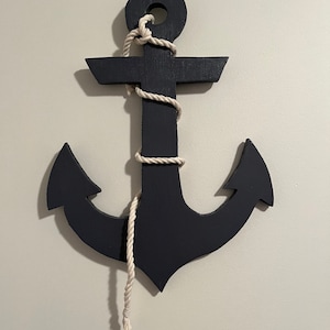 May include: A black wooden anchor with a white rope wrapped around it. The anchor is hanging on a white wall.
