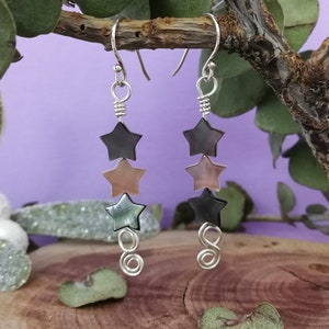 May include: A pair of silver earrings with three black, brown, and iridescent star-shaped charms hanging from each earring.