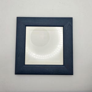May include: A square, navy blue wooden picture frame with a white mount and a circular design in the centre. The frame has a simple, modern design and is set against a white background.