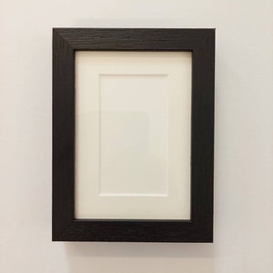 May include: A black wood picture frame with a white mount.