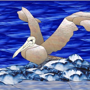 May include: Stained glass artwork showing a pelican in flight over a snowy landscape and blue water. The pelican is in shades of beige and white, with a long beak. The background features deep blue water and white-capped mountains.