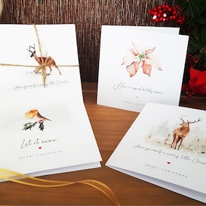 May include: Set of four Christmas cards featuring watercolor illustrations of a deer, a poinsettia, a robin, and a deer in a snowy forest. The cards have the following text: "Have yourself a merry little Christmas", "Have a magical holiday season", "Let it snow", and "Have yourself a merry little Christmas".