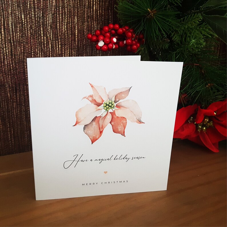 May include: A Christmas card with a watercolor illustration of a poinsettia flower. The card reads "Have a magical holiday season" and "Merry Christmas".