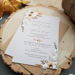 May include: A wedding invitation with a floral design in shades of white, brown, and green. The invitation is for Sophie Coleman and Andrew Harper, and it states that the wedding will take place on Saturday, December 11th, 2024 at 7pm at Woods Lodge, St Paul's Street, Cambridge. The invitation also includes a request for RSVP by May 1st, 2023.
