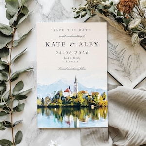 May include: A wedding invitation with the text "SAVE THE DATE" and the names "KATE & ALEX" along with the date "24.06.2026". The invitation features a watercolour painting of a lake with a church and mountains in the background.