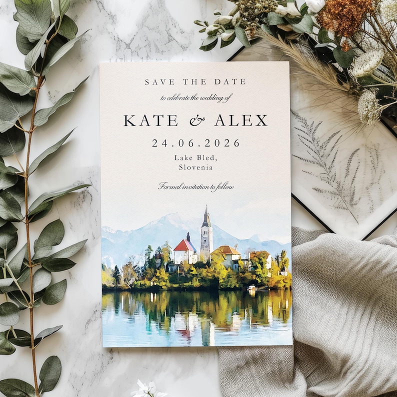 May include: A wedding invitation with the text "SAVE THE DATE" and the names "KATE & ALEX" along with the date "24.06.2026". The invitation features a watercolour painting of a lake with a church and mountains in the background.