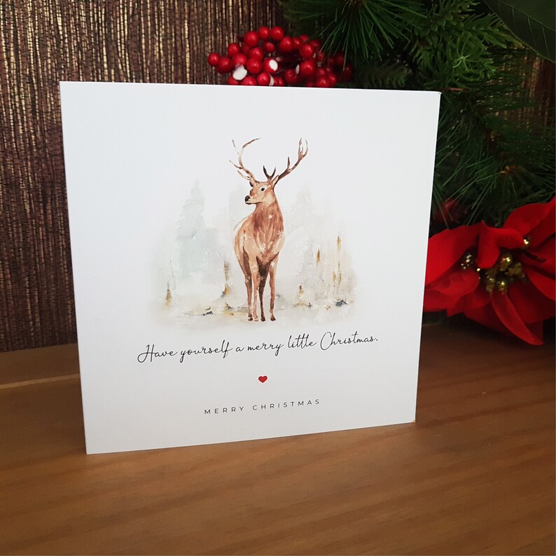 May include: A white Christmas card with a watercolor illustration of a deer in a snowy forest. The card reads "Have yourself a merry little Christmas." with a red heart below the text and "Merry Christmas" at the bottom.
