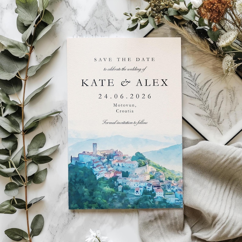 May include: A wedding invitation with the text "SAVE THE DATE" and the names "KATE & ALEX" along with the date "24.06.2026". The invitation features a watercolour painting of a hillside town with a tower.