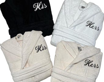 Pode incluir: Quatro roupões em preto, branco e creme. Dois roupões são bordados com "His" em itálico, e dois com "Hers". Os roupões têm golas de xale e cintos a condizer. A imagem é vista de cima.