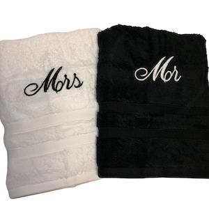 May include: Two matching bath towels, one white and one black. The white towel has "Mrs" embroidered in black script, and the black towel has "Mr" embroidered in white script. Both towels have a decorative band near the bottom.
