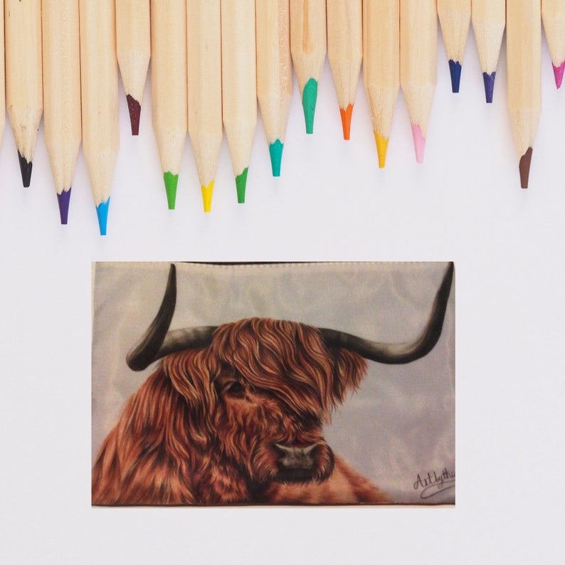 May include: A close-up of a brown and white Highland cow with long, shaggy hair. The cow is looking to the left of the image. The background is a light blue and white watercolor wash. The image is signed "ArtLyth" in the bottom right corner.