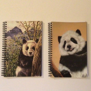 Puede incluir: Dos cuadernos de espiral con ilustraciones de osos panda. El cuaderno de la izquierda tiene un oso panda en un bosque de bambú. El cuaderno de la derecha tiene un oso panda con un fondo blanco.