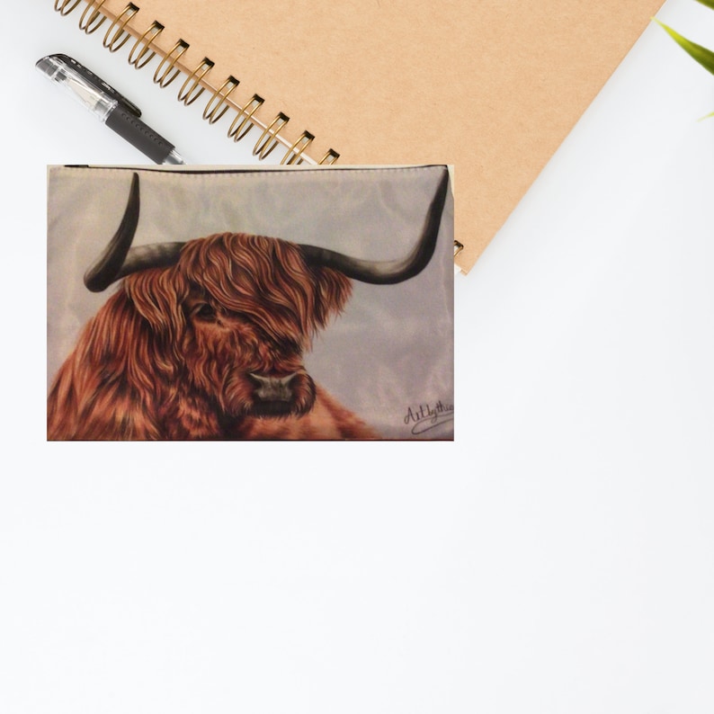 May include: A close-up of a brown and white Highland cow with long, shaggy hair and large horns. The cow is looking to the side, and the background is a light blue.