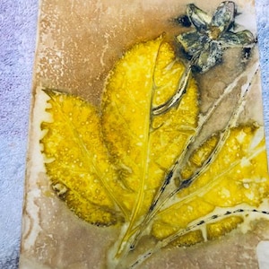 Könnte beinhalten: Ein gepresster Blätter-Kunstdruck mit einem gelben Blatt und einer Blume mit braunem Stiel auf beigefarbenem Hintergrund.