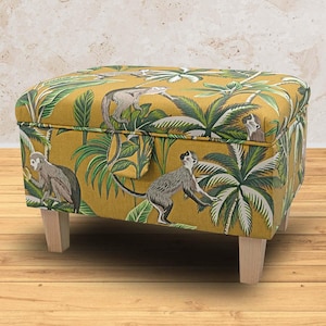 May include: A yellow storage ottoman with a tropical print featuring monkeys and palm trees. The ottoman has wooden legs.