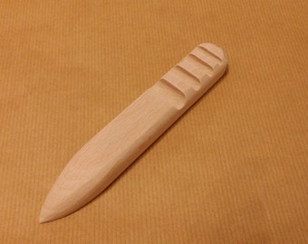 May include: A wooden tool with a pointed tip and a ridged handle. The tool is light brown in color and appears to be handcrafted.