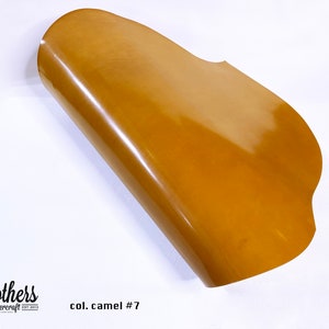 May include: A close-up of a piece of camel colored leather. The leather is folded in half and has a smooth, shiny finish. The text "col. camel #7" is visible in the lower right corner of the image.