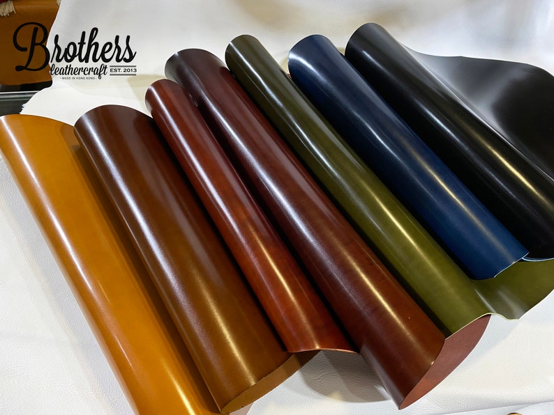 May include: A close-up of six rolls of leather in different colors, including brown, tan, dark brown, green, blue, and black. The leather is rolled up and the edges are visible. The leather is smooth and shiny. The text "Brothers Leathercraft Est. 2013" is visible on the top left corner of the image.