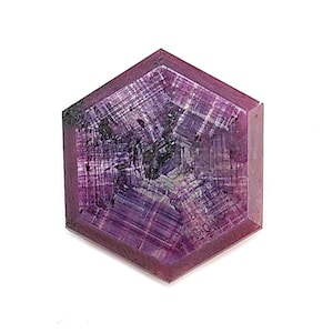 May include: A hexagonal gemstone, deeply purple in colour, with internal patterns of white and black. The gem's facets are clearly defined, and the overall shape is symmetrical. The gem is a striking example of natural beauty.