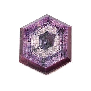 May include: A hexagonal gemstone with a deep purple colour. The gem has a complex internal pattern with shades of white, grey, and black, creating a unique visual texture. The gem is set against a white background.