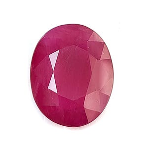 Puede incluir: Una gema de rubí de talla ovalada, que muestra un tono rojo intenso. La superficie facetada refleja la luz, mostrando la claridad y el brillo de la gema. El rubí está sobre un fondo blanco liso, resaltando su color y forma.