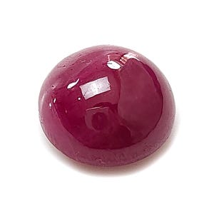 Può includere: Una pietra preziosa rotonda tagliata a cabochon con un colore magenta-rosso profondo e saturo. La superficie è liscia e lucida, con una finitura ad alta brillantezza che riflette la luce, mettendo in risalto la qualità traslucida e la tonalità.