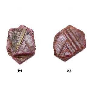 May include: Two rough-cut ruby gemstones with a deep red hue. The stones have visible natural lines and textures, with a mix of dark and lighter red tones. The gemstones are labeled P1 and P2.