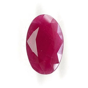 May include: A loose, oval-shaped ruby gemstone with a deep, saturated magenta-red color. The stone features a faceted surface with multiple triangular and trapezoidal cuts that reflect light, creating distinct highlights and shadows across its face.