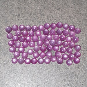 Op de afbeelding: Een verzameling van talrijke kleine, ronde, cabochon geslepen edelstenen in een levendige magenta-roze tint. Elke steen heeft een glad, gepolijst oppervlak met een subtiele reflectie, gerangschikt in een losse, rechthoekige clusterformatie.