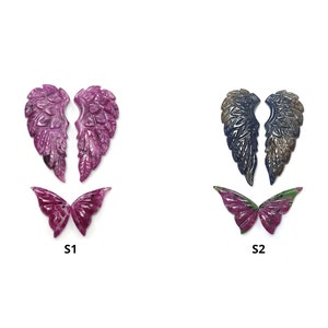 May include: Two sets of carved gemstone wings and butterflies. One set is a deep magenta colour, and the other is a mix of dark blue and bronze. The text "SAKSHAM GEMS THE EFFICACY" is at the top.