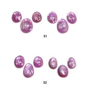 May include: An assortment of oval-shaped, faceted pink gemstones, arranged in two groups labeled S1 and S2. The gemstones have a polished, reflective surface, and are set against a white background. The Saksham Gems logo is at the top.