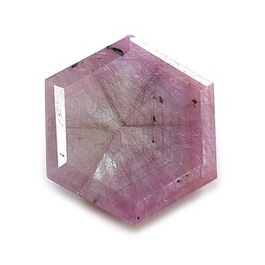 Puede incluir: Una piedra preciosa hexagonal de color rosa con apariencia translúcida, que presenta inclusiones internas visibles y una superficie facetada. La piedra muestra un tono rosa claro con vetas rosa oscuro y pequeñas manchas oscuras.