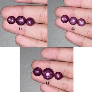 Puede incluir: Tres conjuntos de tres rubíes estrella redondos de color magenta intenso, etiquetados como S1, S2 y S3. Cada piedra preciosa tallada en cabujón muestra un efecto de estrella de seis rayos, llamado asterismo, en la superficie pulida.